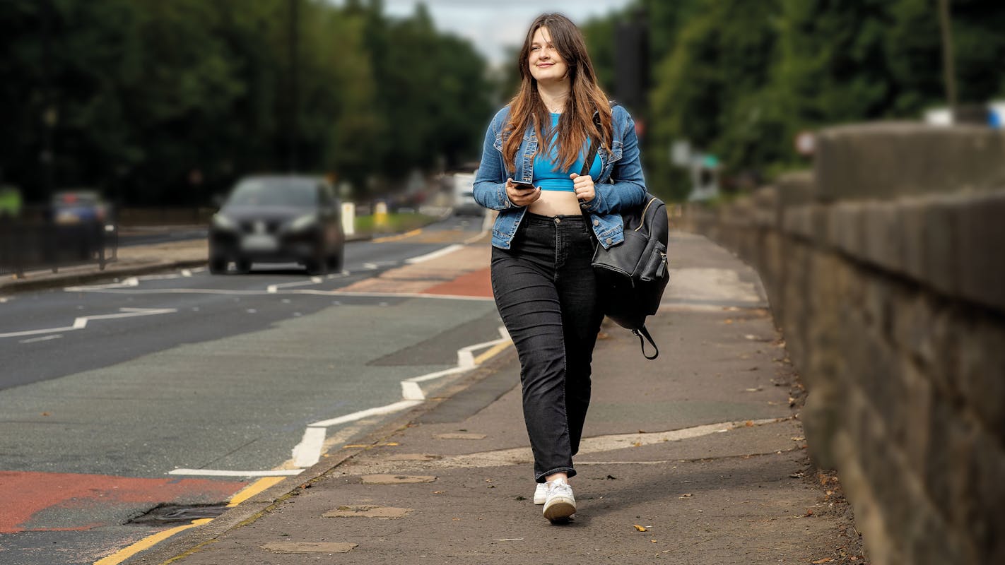 A woman walks next to a road.