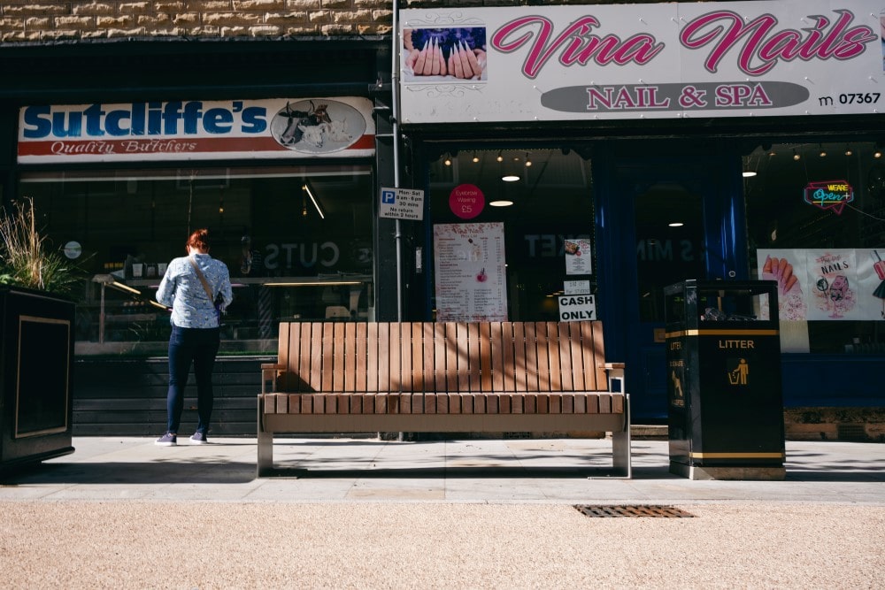 A smart metal and wooden bench outside shops in Elland.